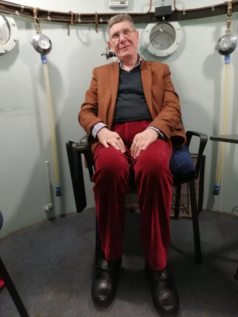 Christopher Fox-Walker seated in a multiplace hyperbaric chamber at the Sussex MS Centre